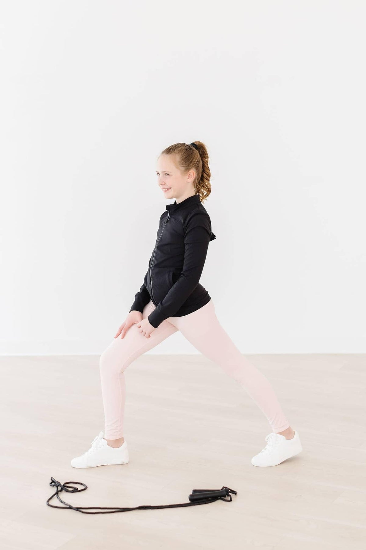 Young girl wearing pink girls active leggings stretching with jump rope on floor