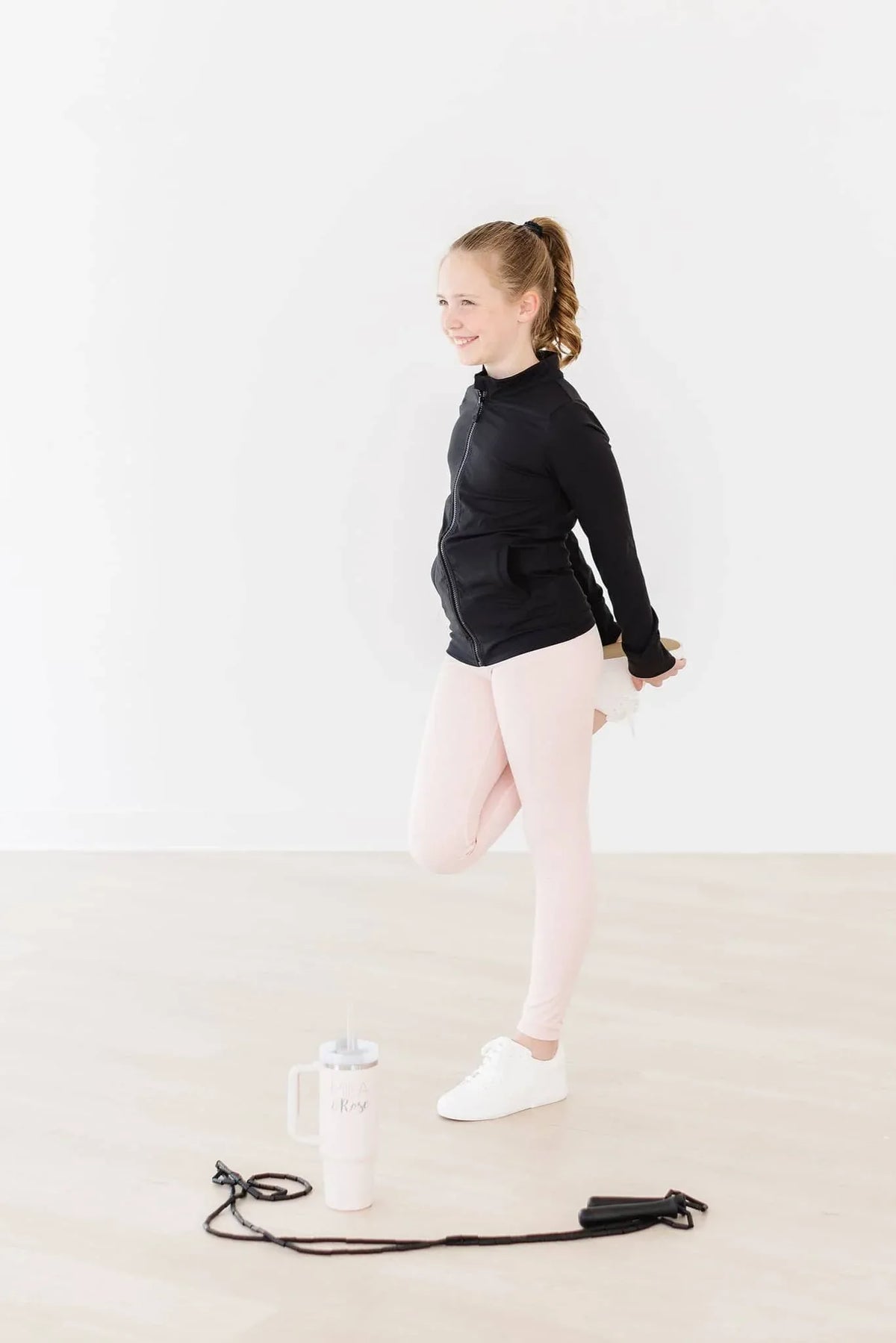 Young girl stretching wearing pink girls active leggings and black jacket in workout studio