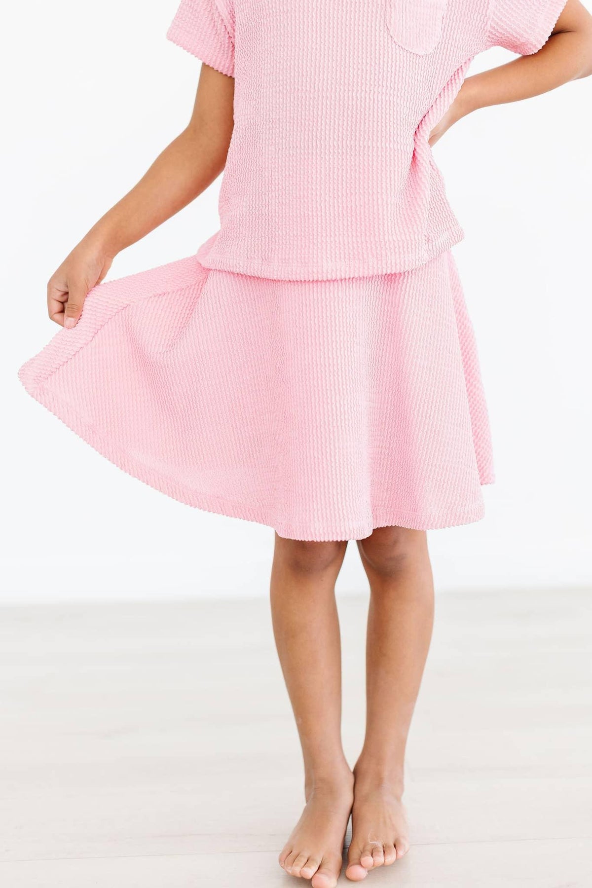 girl wearing girls bubblegum pink twirl skort holding hem while standing barefoot