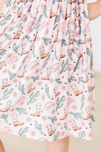 girl wearing pink girls cactus twirl dress with cowboy boot and cactus print holding dress sides