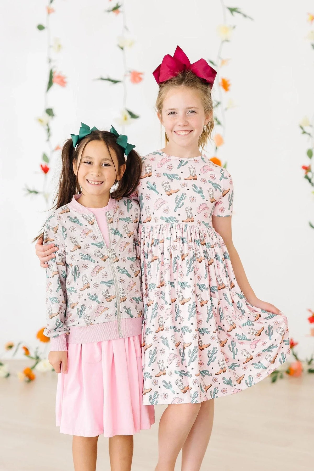 Two girls smiling wearing girls cactus twirl dress and matching cactus jacket with colorful bows