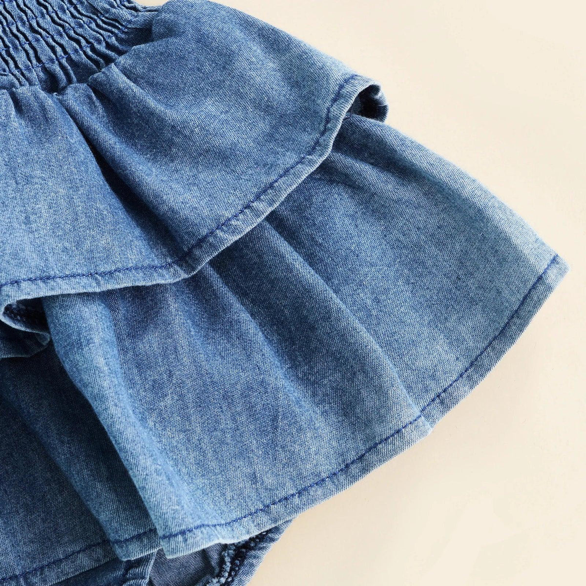 close-up of blue girls denim romper 0-24 months showing ruffled skirt detail and fabric texture