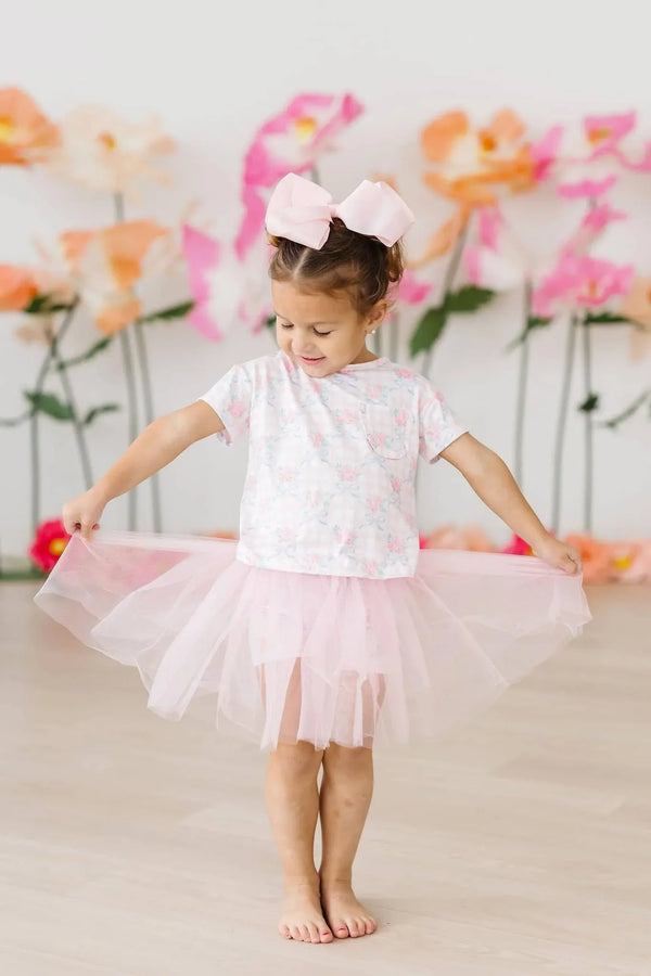 Toddler girl wearing white and pink girls floral ruffle pocket tee with pink tutu skirt holding skirt out