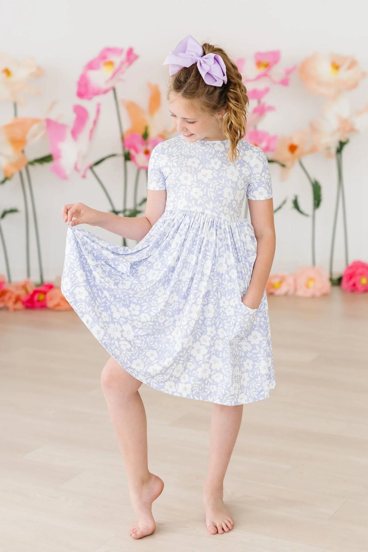 Girls floral twirl dress in light blue and white with short sleeves, pocket detail, worn by young girl