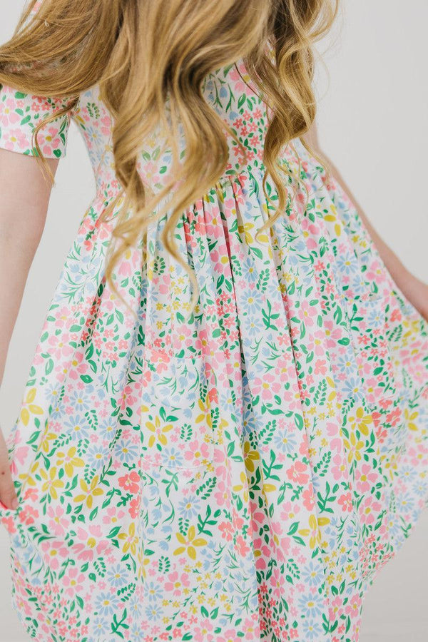 Young girl wearing a pink and green girls floral twirl dress holding out the skirt