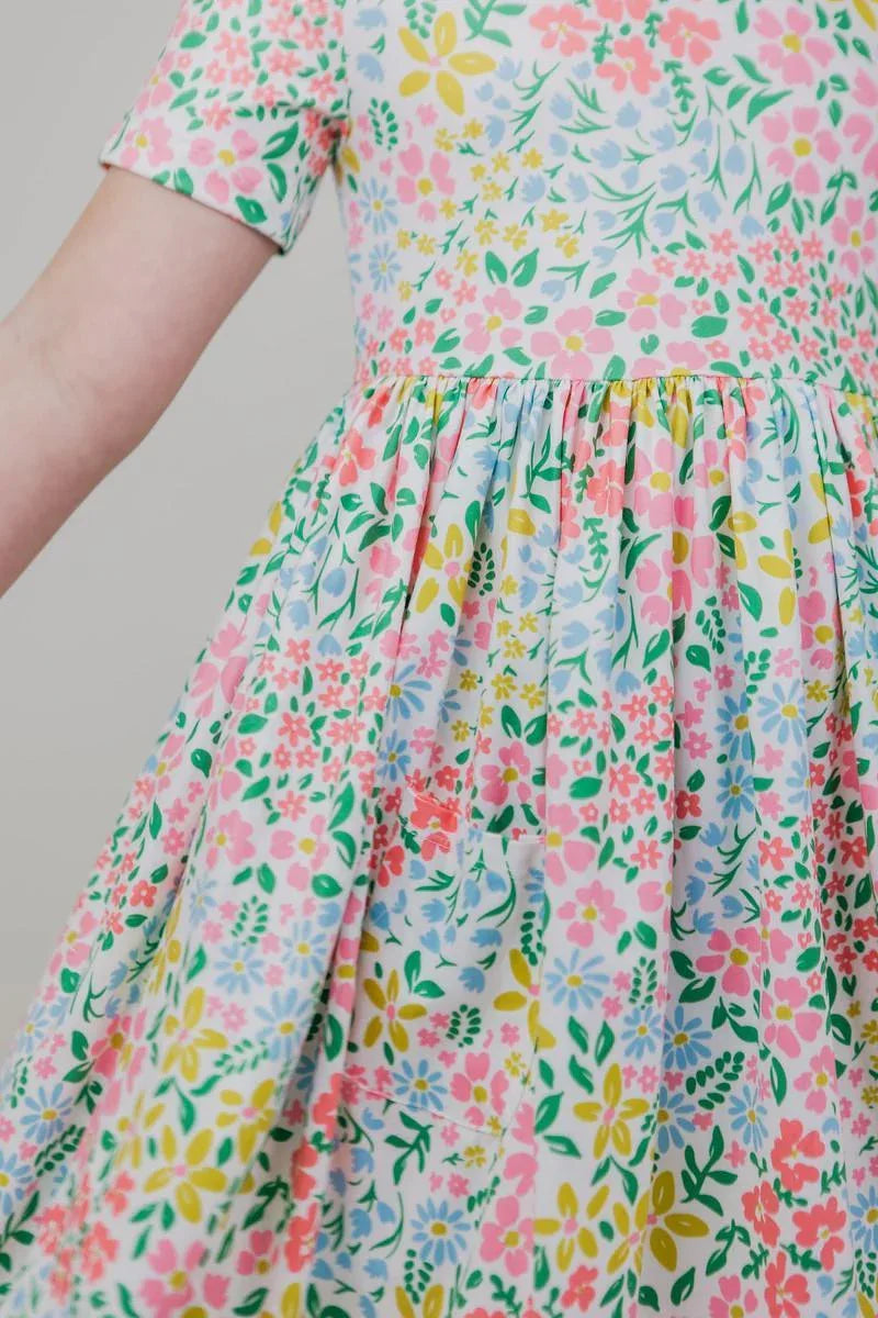 girl wearing pastel pink and multicolor girls floral twirl dress spreading her arms