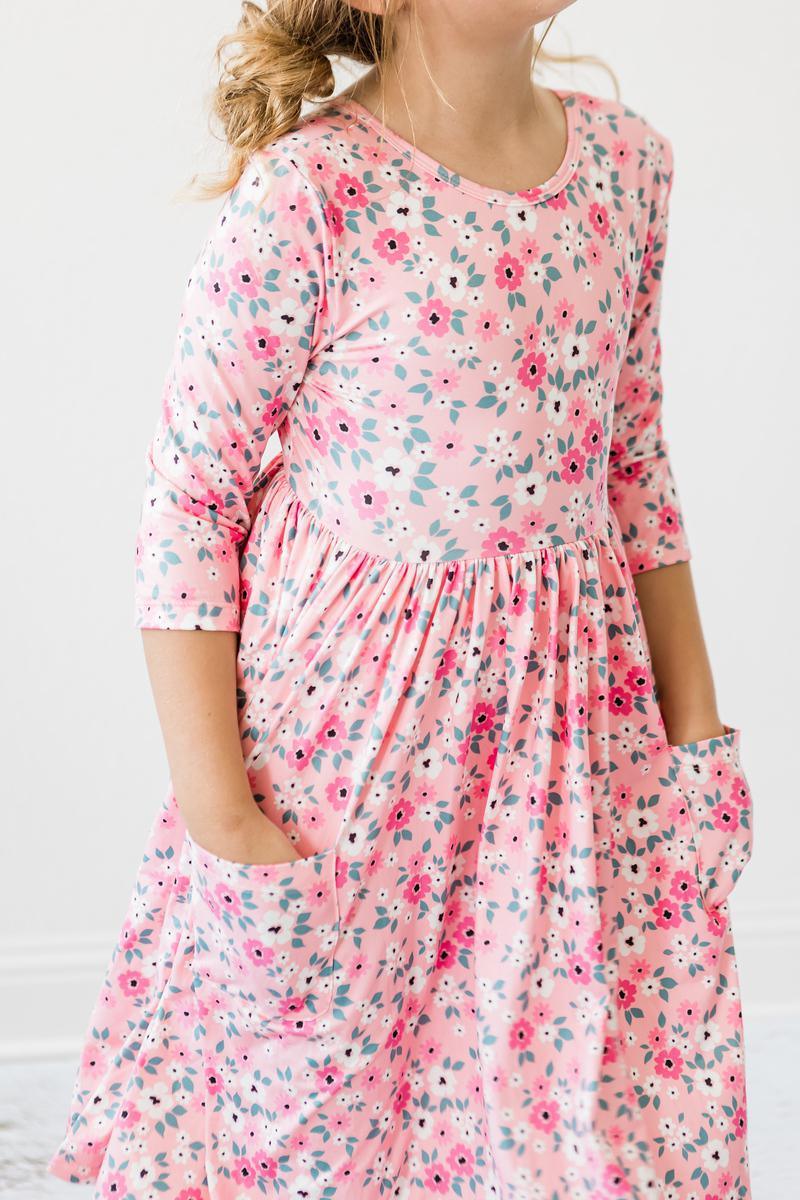 young girl wearing pink girls floral twirl dress with three quarter sleeves and pockets posing with hands in pockets