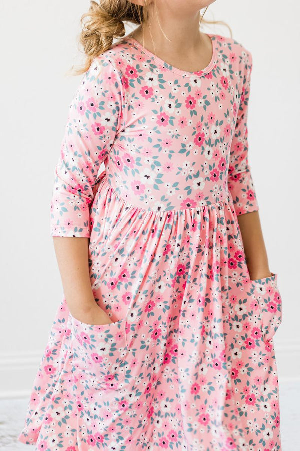 young girl wearing pink girls floral twirl dress with three quarter sleeves and pockets posing with hands in pockets