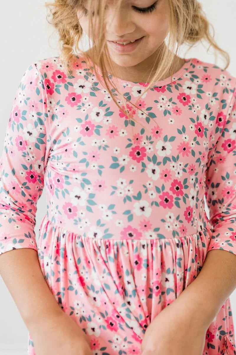 Young girl wearing pink girls floral twirl dress with 3/4 sleeves smiling and looking down