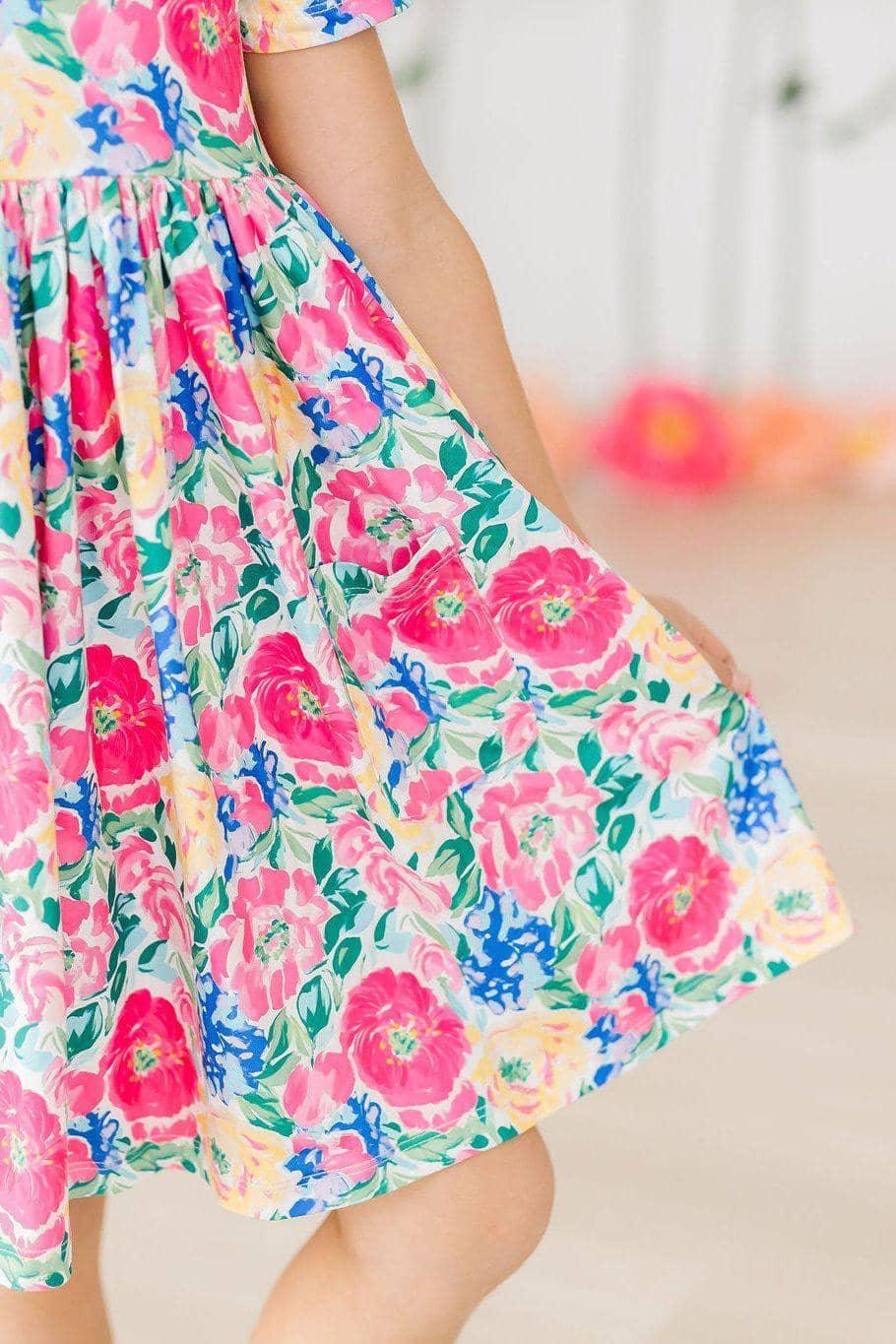 young girl wearing colorful girls floral twirl dress holding the skirt while twirling indoors