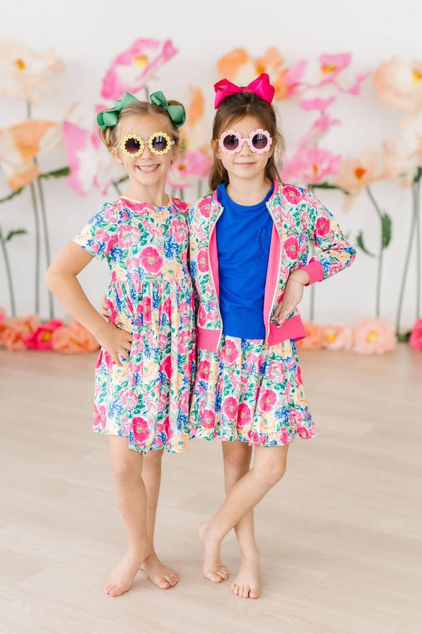 Two girls wearing colorful girls floral twirl dress, one posing with hands on hips and the other with crossed legs