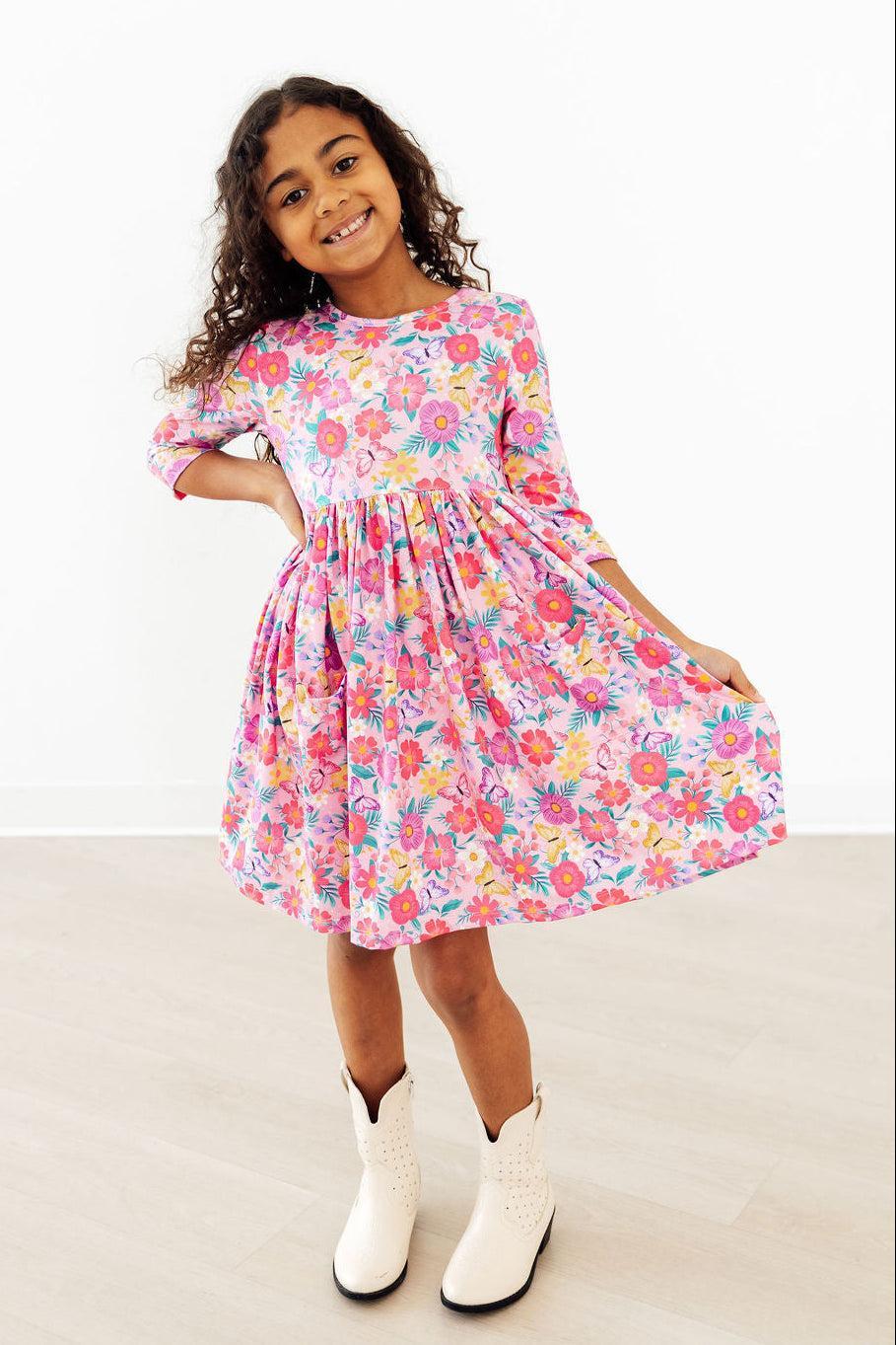 Young girl wearing pink girls floral twirl dress with sleeves smiling and holding dress