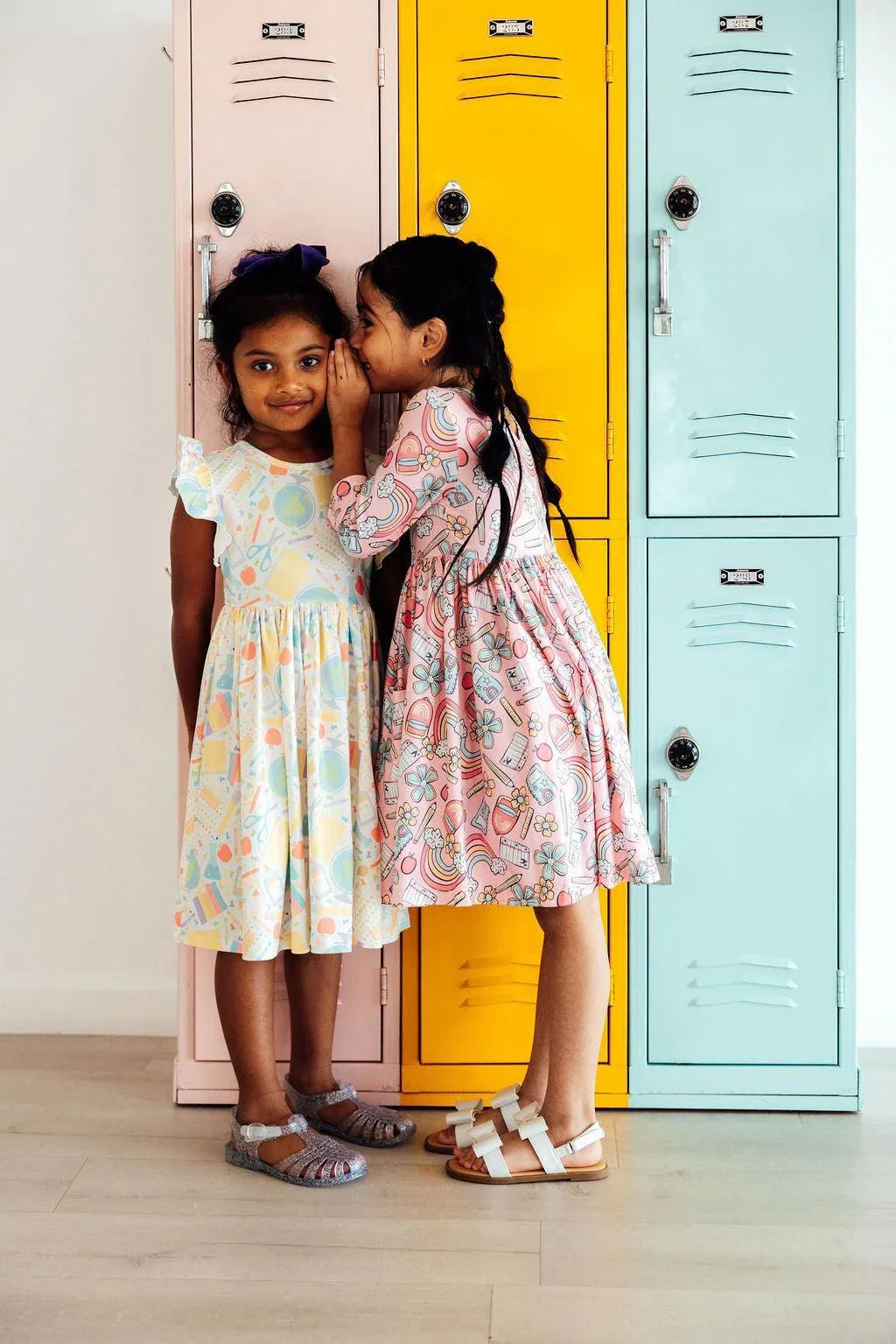Two girls wearing pastel girls flutter sleeve twirl dresses with colorful patterns standing by lockers