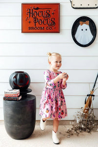 toddler girl wearing pink girls Halloween twirl dress holding pumpkin near Halloween decorations