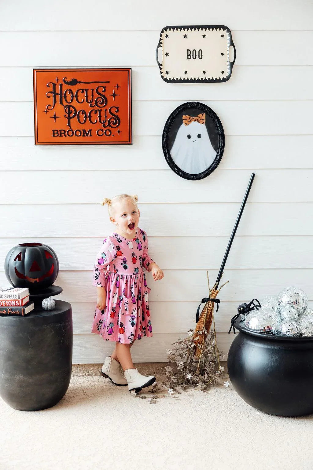 young girl wearing pink girls Halloween twirl dress with pumpkins twirling indoors by Halloween decor
