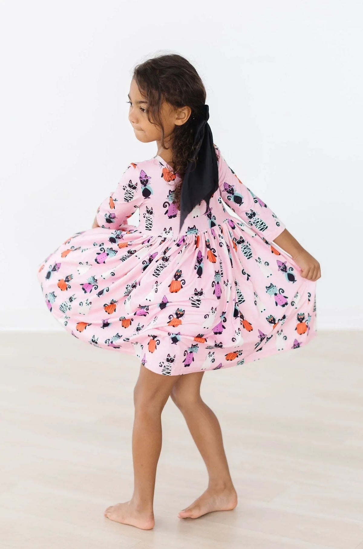 Young girl wearing pink girls Halloween twirl dress with pumpkins and bats twirling barefoot indoors