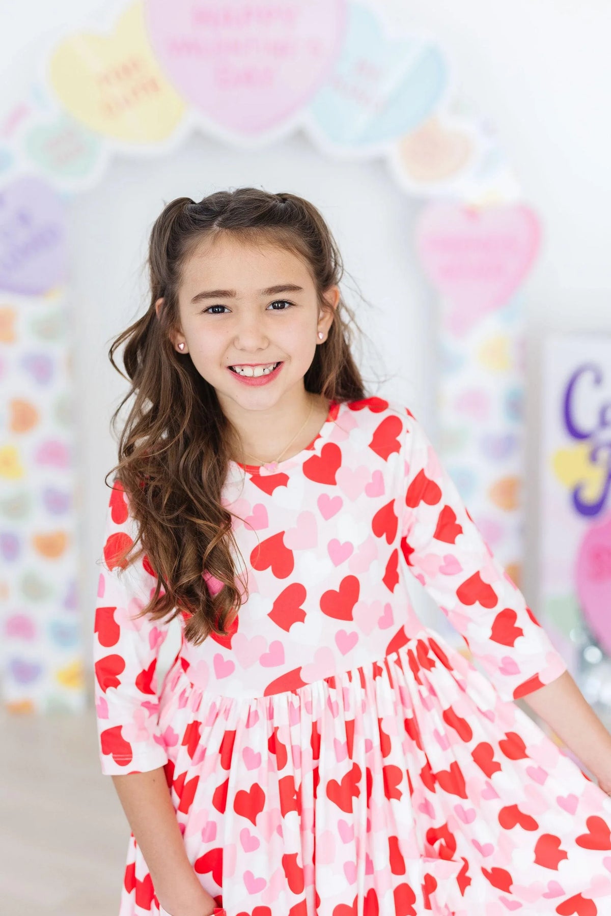 young girl wearing a pink and red girls heart print twirl dress smiling and twirling indoors