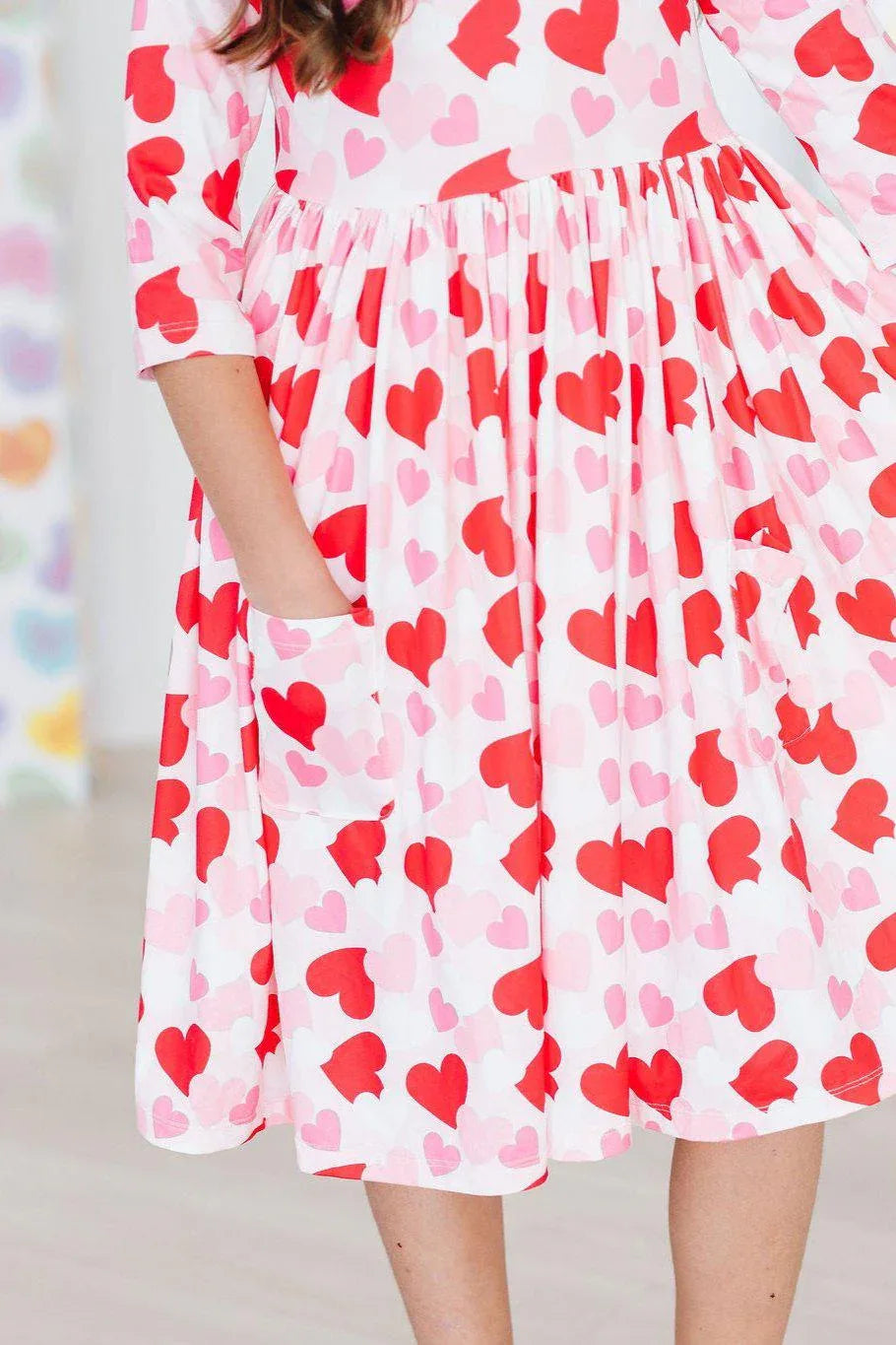 Girl wearing Mila Rose girls heart print twirl dress in red and pink holding pocket