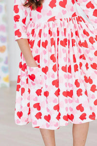 Girl wearing Mila Rose girls heart print twirl dress in red and pink holding pocket