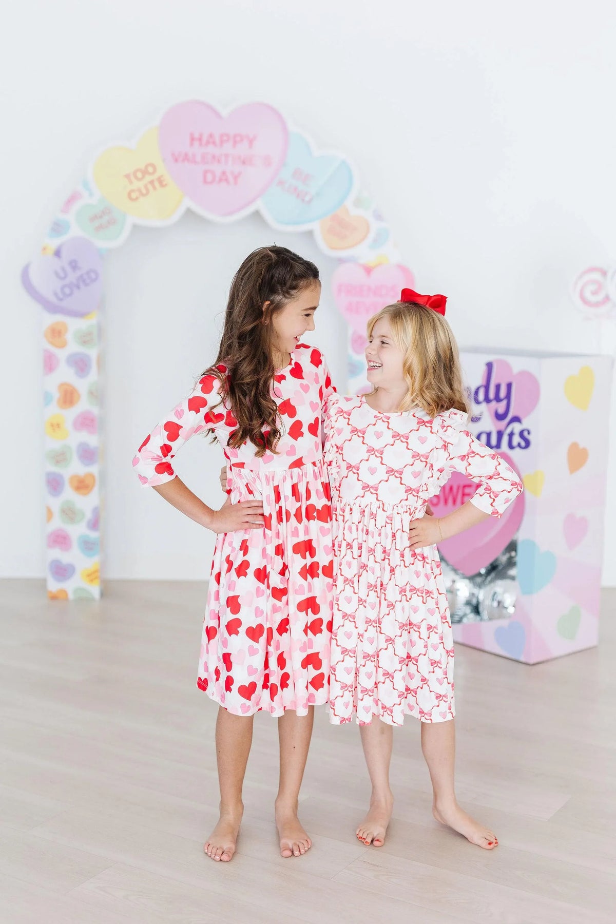 Two girls wearing girls heart print twirl dress in red and white standing barefoot smiling