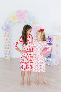 Two girls wearing girls heart print twirl dress in red and white standing barefoot smiling