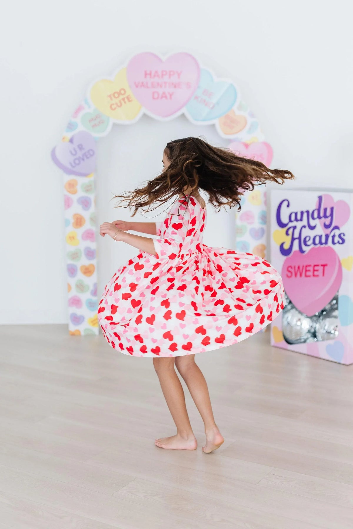 Young girl twirling in a red and white girls heart print twirl dress with 3/4 sleeves indoors