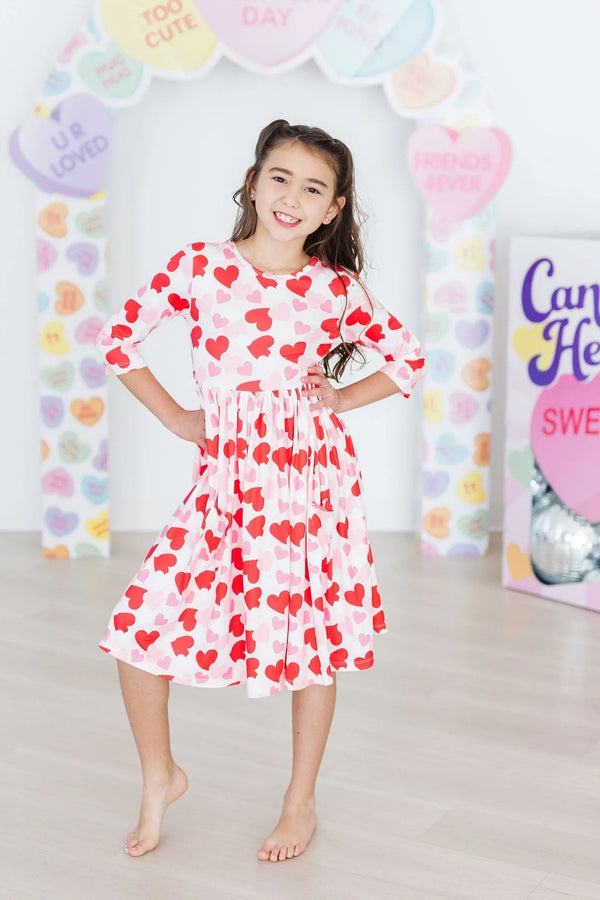 girl wearing girls heart print twirl dress in white with red hearts smiling and twirling indoors