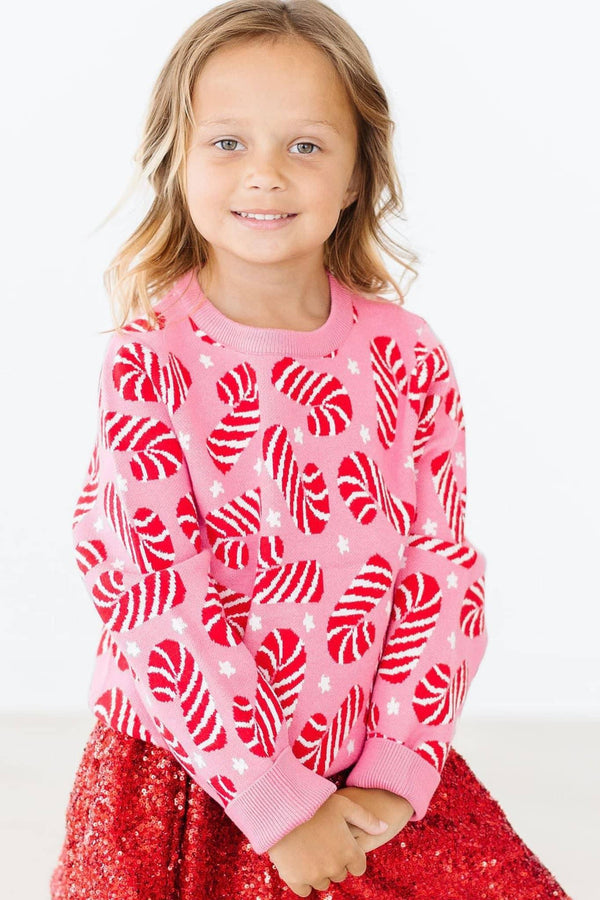Young girl wearing pink girls holiday candy cane sweater sitting with hands folded