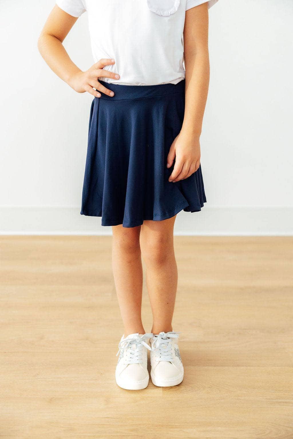 Girl wearing girls navy skort with shorts standing with hand on hip in white shirt and sneakers