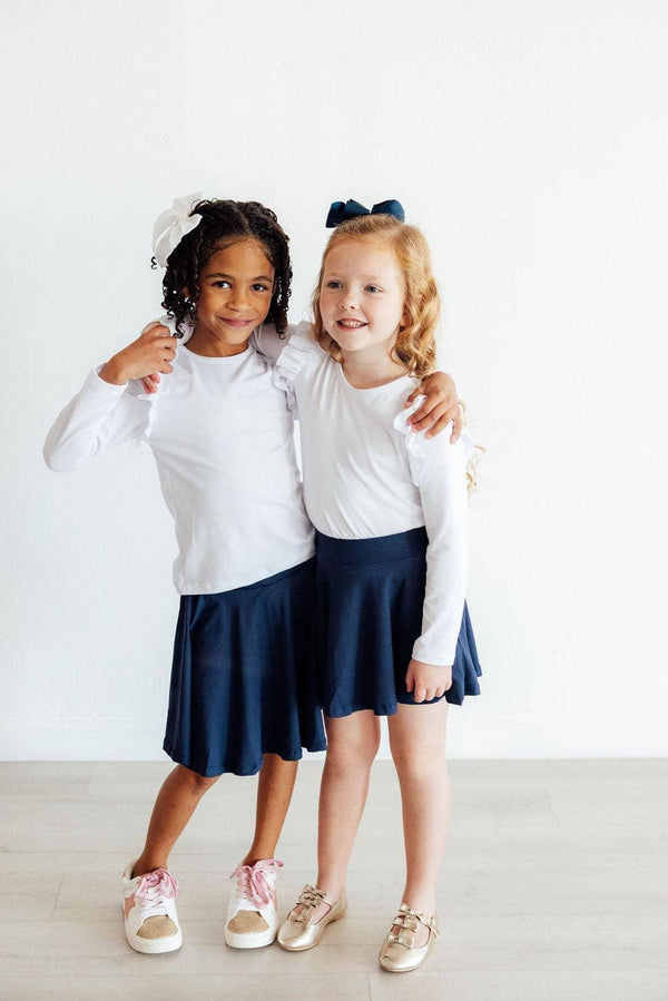 Two young girls wearing girls navy skort with shorts and white long sleeve shirts smiling and posing together