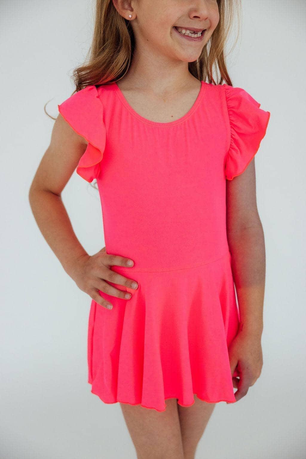Young girl wearing girls neon pink twirl leotard standing with hand on hip smiling