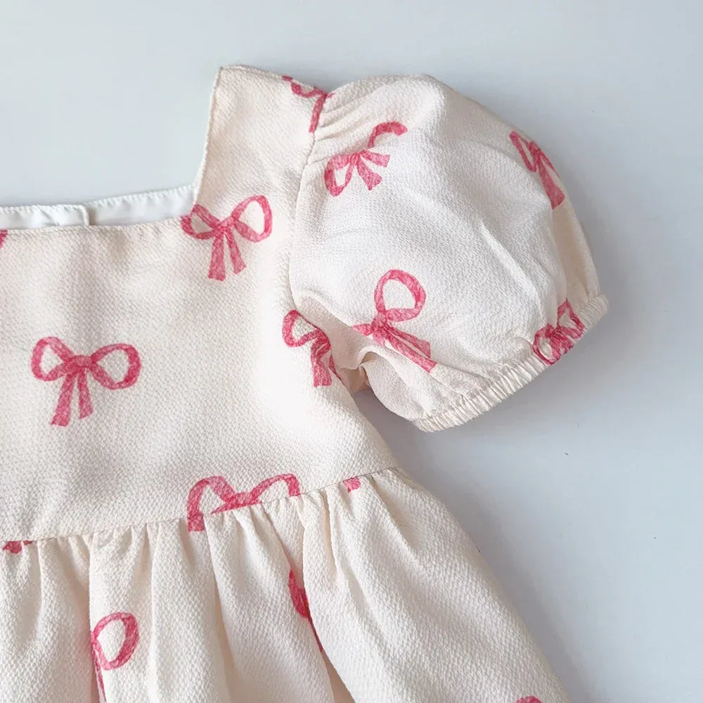 Girls pink party dress with puff sleeves featuring textured white fabric and pink bow prints