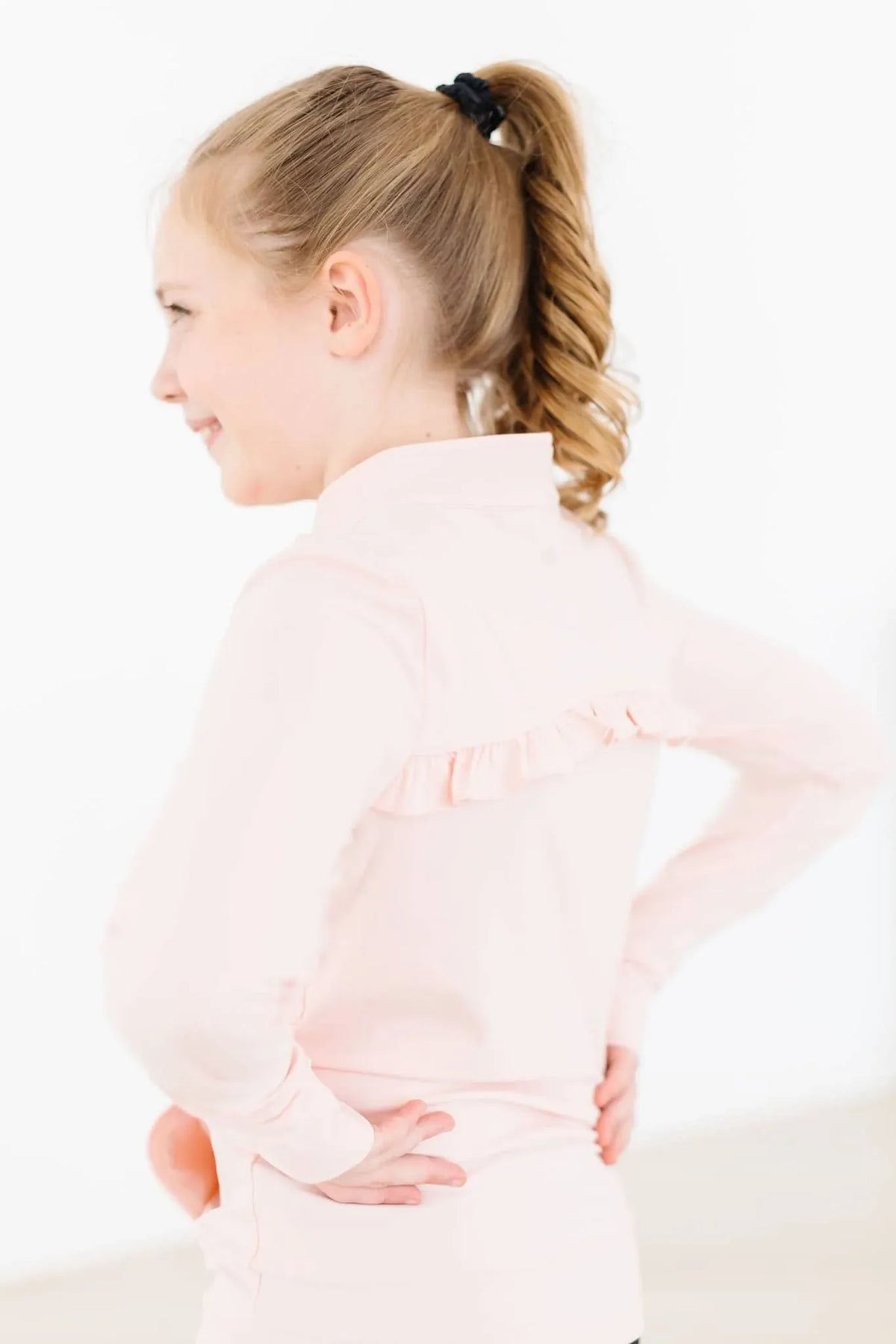 Young girl wearing girls pink ruffle zip jacket standing with hands on hips in profile