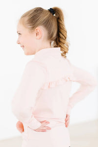 Young girl wearing girls pink ruffle zip jacket standing with hands on hips in profile