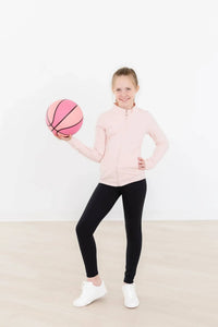 Young girl wearing girls pink ruffle zip jacket holding a pink basketball and smiling