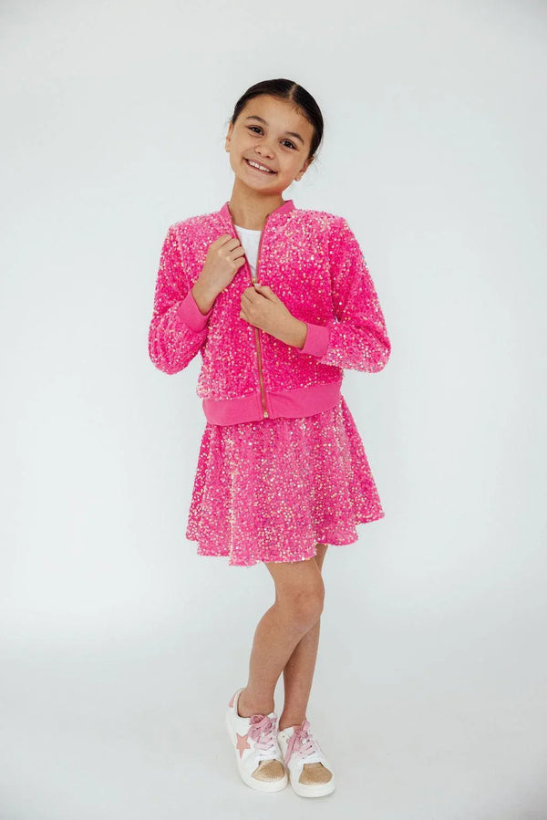 Girl wearing girls pink sequin skort and matching jacket smiling with hands holding jacket collar