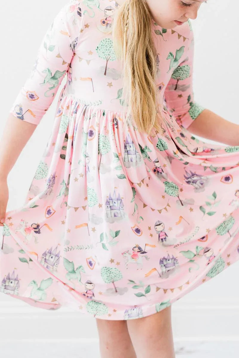 Young girl wearing pink girls pocket twirl dress with castle and tree prints holding skirt out