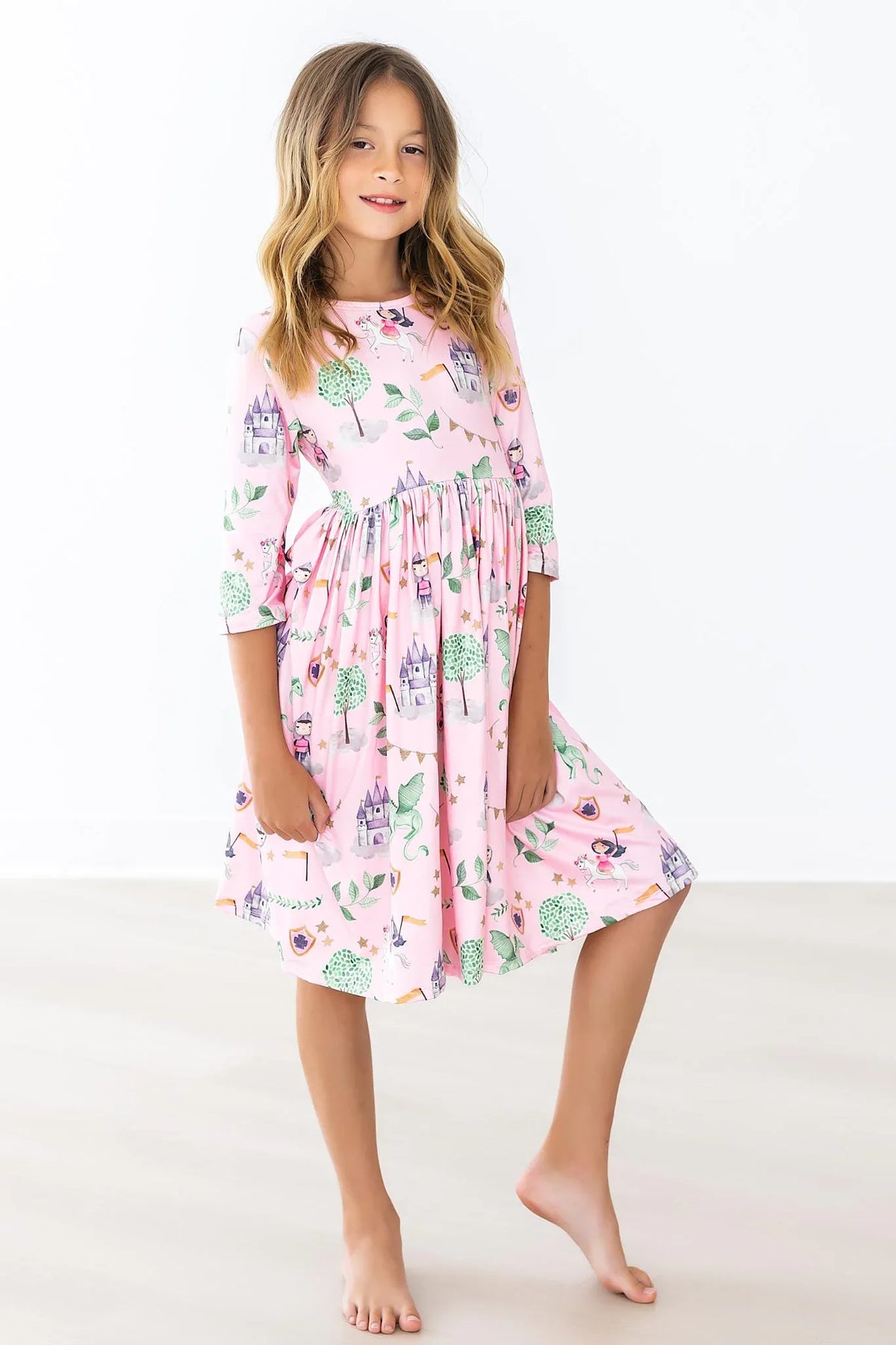 Young girl wearing pink girls pocket twirl dress with trees and castle print standing barefoot