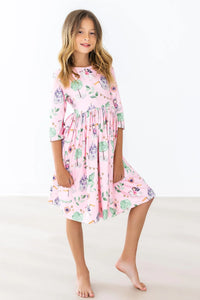 Young girl wearing pink girls pocket twirl dress with trees and castle print standing barefoot