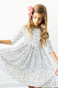 Young girl wearing white and black girls polka dot twirl dress with 3/4 sleeves holding dress out