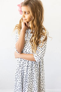 Girl wearing white and black girls polka dot twirl dress with 3/4 sleeves standing with hand near chin