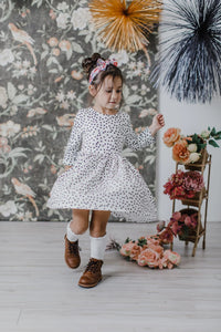 Young girl wearing white and black girls polka dot twirl dress with 3/4 sleeves dancing indoors
