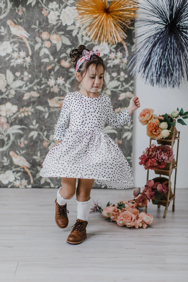 Young girl wearing white and black girls polka dot twirl dress with 3/4 sleeves dancing indoors