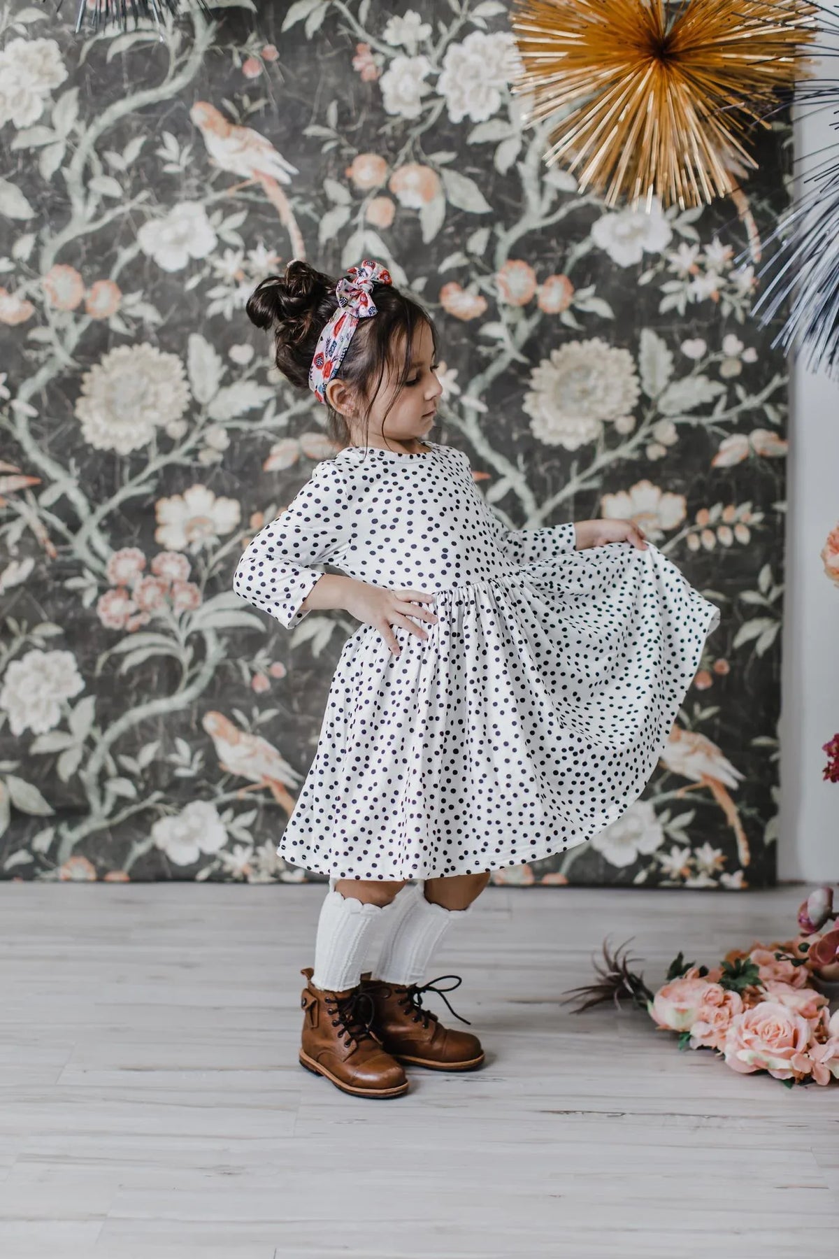 Young girl wearing white girls polka dot twirl dress standing sideways and holding the skirt