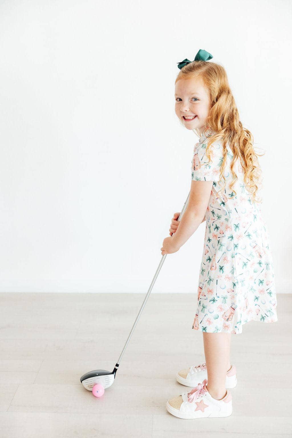 young girl wearing white girls polo dress with floral print playing with pink golf ball