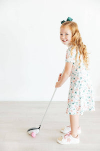 young girl wearing white girls polo dress with floral print playing with pink golf ball