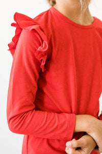 girl wearing girls red ruffle long sleeve top with ruffled shoulder detail standing with arms crossed