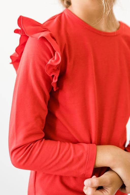girl wearing girls red ruffle long sleeve top with ruffled shoulder detail standing with arms crossed