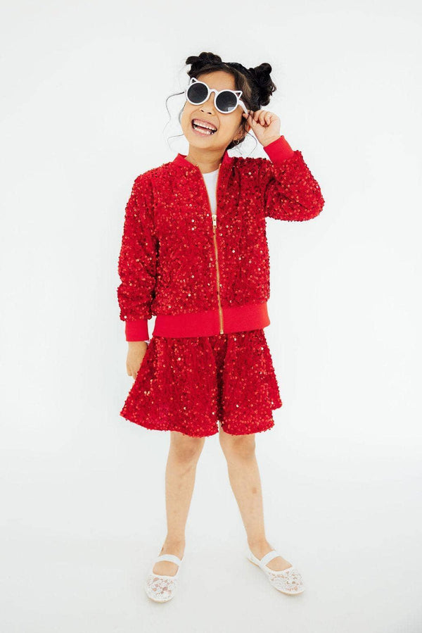 Girl wearing girls red sequin skort and matching jacket smiling and posing with sunglasses