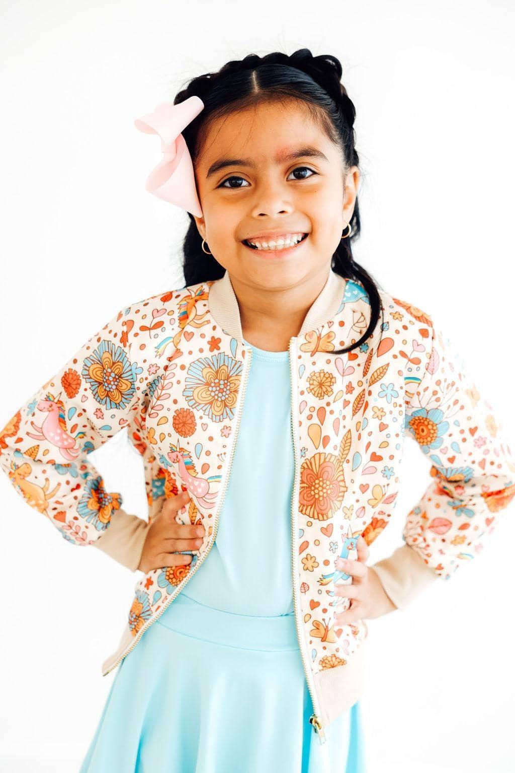 Girls retro unicorn satin jacket with floral print on cream background, worn by young girl with pink bow